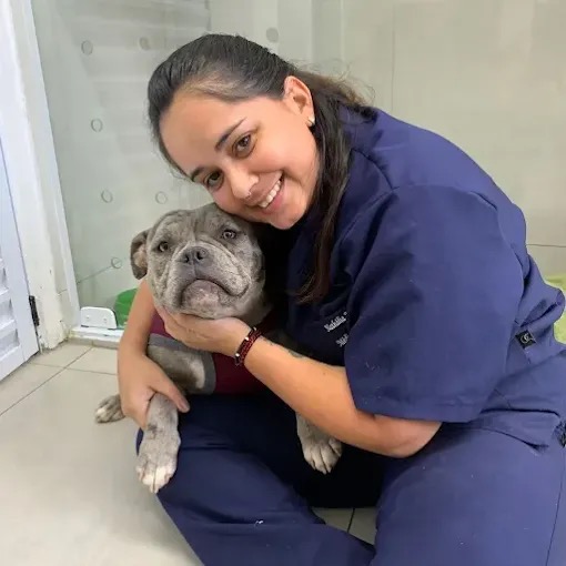 Veterinária Zenvet abraçando um cão pitbull cinza, sentada no chão da clínica